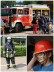 Feuerwehrauto mit geöffneten Fächern sowie ein Feuerwehrmann in vollter Montur und ein geschminktes Kind mit Feuerwehrhelm auf dem Kopf.