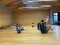 Fünf Kindergartenkinder und ein Mann sitzen in einem großen Raum auf dem Boden. Alle tragen sportliche Kleidung. Sie haben teilweise die Beine und Arme in der Luft und bewegen sich im Kreis. 